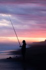 Силует чоловіка риболовля на березі моря на заході сонця — стокове фото