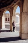 Повна задоволена жінка-туристка в традиційному східному одязі посміхається перед камерою, стоячи на вході до старого будинку з колонами та арками в Катарі. — стокове фото