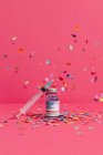 Коронавирусная вакцина колба возле шприца с иглой на розовом фоне покрыта конфетти — стоковое фото