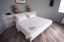 Chambre d'hôtel Maldives avec lit en draps blancs avec des lettres en feuilles de bambou écrit bienvenue à la maison — Photo de stock