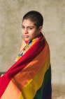 Serious young bisexual ethnic female with multicolored flag representing LGBTQ symbols and looking at camera on sunny day — Stock Photo