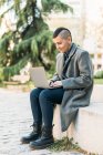 Androgynous pessoa com mohawk em botas e casaco de surf internet no netbook enquanto sentado na cidade — Fotografia de Stock