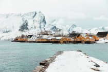 Kaltes Meer mit ruhigem Wasser in der Nähe von Küstensiedlungen und schneebedecktem Gebirgskamm an bewölkten Wintertagen auf den Lofoten, Norwegen — Stockfoto