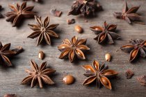 Primer plano de estrellas aromáticas de anís seco con semillas esparcidas sobre una mesa rústica de madera para el concepto gastronómico de fondo - foto de stock