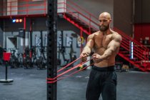 Homem barbudo muscular puxando corda elástica com esforço durante o treino funcional no ginásio moderno — Fotografia de Stock