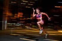 Vista lateral da mulher atlética afro-americana muscular correndo na rua turva à noite — Fotografia de Stock