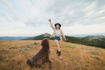 Двухлетняя хозяйка с деревянной палкой, бегающая на лапах и играющая с собакой лабрадора, веселясь вместе в горах — стоковое фото