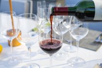 Официант наливает красное вино в бокал в ресторане высокой кухни на открытом воздухе — стоковое фото