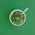 Сверху здоровый салат с зеленой фасолью и ломтиками чеснока в миске подается на зеленом столе — стоковое фото