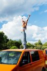 Side view of carefree female traveler standing on roof on van parked in nature in summer — Stock Photo