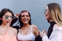 Positive female friends in trendy sunglasses and casual clothes laughing happily while spending pleasant time together — Stock Photo