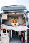 Happy African American female with curly hair smiling and browsing cellphone while resting on bed in caravan during road trip — Stock Photo