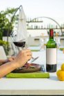 Botella de vino y cliente sosteniendo una copa en el restaurante de alta cocina al aire libre - foto de stock