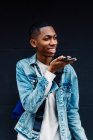 Seitenansicht eines jungen schwarzen Mannes mit Handy und Rucksack auf der Straße, während er eine Sprachnachricht hinterlässt — Stockfoto