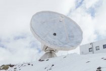 From below of satellite antenna on snowy mountain against building facade under cloudy sky in Spain — Stock Photo