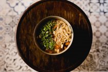 Сверху керамическая чаша с китайской раменной едой на круге деревянный поднос на восточном фоне украшения — стоковое фото