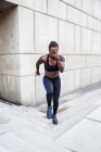 Fuerte mujer afroamericana corriendo escaleras arriba mientras entrenaba cerca de un edificio moderno en la calle de la ciudad - foto de stock