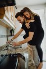 Веселий бородатий чоловік обіймає усміхнену жінку, спираючись на шафу з раковиною в затишній кухні вдома — стокове фото