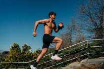 Seitenansicht eines aktiven männlichen Joggers mit nacktem Oberkörper, der beim Training unter blauem Himmel auf der Treppe läuft — Stockfoto