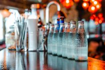 Glasflaschen mit kaltem Erfrischungswasser reihenweise auf Holztheke in Bar platziert — Stockfoto