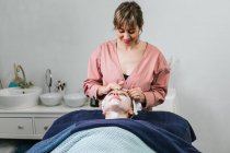 Жіночий косметолог наносить засоби для чищення обличчя на обличчя жіночого клієнта під час догляду за шкірою в салоні краси — стокове фото