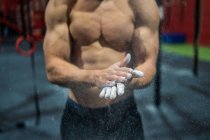 Unrecognizable muscular athlete spreading chalk on hands during weightlifting workout in gym — Stock Photo