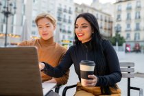 Freelancer multirracial alegre sentado à mesa com laptop e trabalhando em projeto remoto juntos no café ao ar livre — Fotografia de Stock
