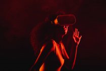 Mujer étnica anónima explorando la realidad virtual en auriculares sobre fondo negro - foto de stock
