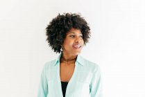 Heureuse jeune femme afro-américaine avec de beaux cheveux afro en tenue tendance regardant loin sur fond blanc — Photo de stock