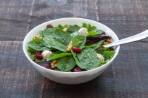 Hoher Winkel von köstlichem Salat mit Spinat und Bohnen und Walnüssen serviert in einer Schüssel auf einem Holztisch für ein gesundes Mittagessen — Stockfoto