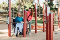 Zufriedene erwachsene Frau hilft Seniorin im Rollstuhl bei Übungen auf Sportplatz während Reha-Sitzung — Stockfoto