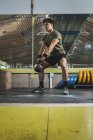 Азіатський чоловік тренує плечі й руки з важкими кетлебелами в спортзалі під час функціонального тренування й озирається геть — стокове фото