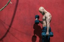 Вид збоку сильного бородатого спортсмена, який дивиться з важкими гантелями, що ходять у сучасному тренажерному залі під час тренувань з важкої атлетики — стокове фото