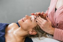 Обрезанная неузнаваемая массажистка массирует плечи клиентки лежащей на столе в салоне красоты — стоковое фото