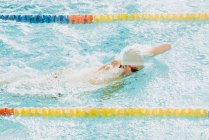 Side view of paralympic sportsman in goggles and cap without hand swimming crawl style in pool between lanes — Stock Photo