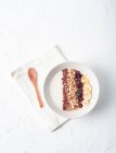 Вид зверху миски з білим йогуртом увінчаний різноманітними злаками і нарізаним бананом, який подається для здорового сніданку на столі з дерев'яною ложкою — стокове фото