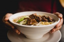 Gros bol de délicieuse soupe de nouilles asiatiques avec côtes de porc placé sur la table de café — Photo de stock