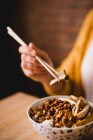 Manos de mujer comiendo con palillos de cerámica tazón de delicioso plato Lu Rou ventilador con tofu colocado en la mesa en la cafetería - foto de stock