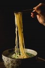Mano di donna che tiene bacchette di bambù con gustose tagliatelle di grano dal piatto di farina di ramen cinese — Foto stock