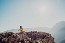 Vue latérale d'une voyageuse anonyme assise sur le rocher dans les hautes terres et faisant du yoga à Padmasana — Photo de stock