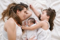 Von oben lächelnde Mutter und kleines Mädchen, die mit niedlichem Säugling im Bett liegen — Stockfoto