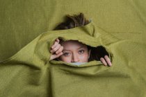 Молода зеленоока жінка дивиться на камеру, ховаючись за рваною зеленою тканиною — стокове фото