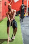 Sportif fort tirant la corde avec des poids lourds pendant l'entraînement intense dans la salle de gym contemporaine — Photo de stock