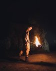 Вид збоку молодого чоловіка спелеолог з палаючим факелом, що стоїть у темній вузькій скелястій печері, досліджуючи підземне середовище — стокове фото