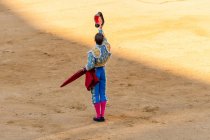 Back view of unrecognizable bullfighter in fancy costume taking off hat after corrida performance while standing on sandy arena — Stock Photo