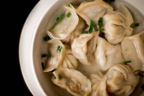 Closeup bowl of delicious soup with dumplings and spring onion against black background — Stock Photo