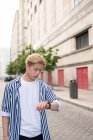Serious ethnic male checking time on wristwatch while standing in street and waiting for meeting — Stock Photo