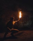 Unrecognizable male adventurer with bright burning torch crouching while exploring dark underground cave during speleology expedition — Stock Photo