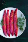 From above gravlax with mixed peppercorns and fresh dill sprigs on plate on dark background — Stock Photo