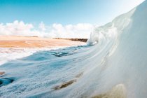 Ondas marinhas espumosas poderosas rolando e salpicando sobre a superfície da água contra o céu azul — Fotografia de Stock